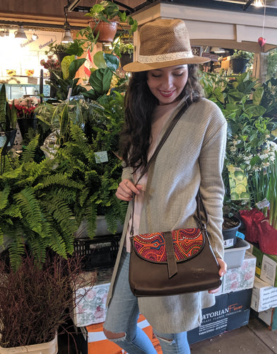 Woman looking down at her medium crossbody bag with mola design over her shoulder. 