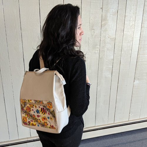 Woman with dark hair and a white backpack with hand painted and hand stamped decoration